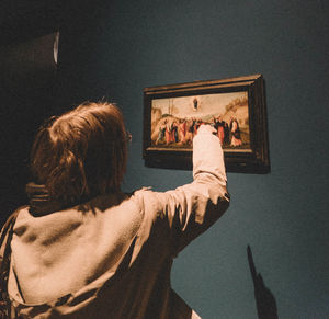 Rear view of woman pointing towards panting on wall