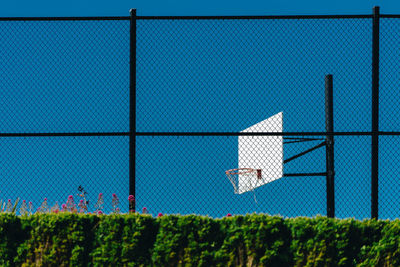 Basketball hoop against clear sky seen through chainlink fence