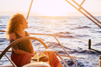 Side view of woman sitting on sailboat in sea