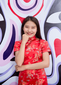 Portrait of a smiling young woman standing against wall