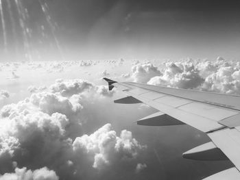 Cropped image of aircraft wing flying over clouds against sky