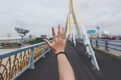 Cropped hand of woman on bridge against sky in city