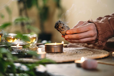 Woman hands burning white sage, before ritual on the table with candles and green plants. smoke of