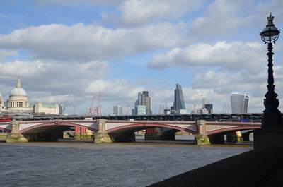 Bridge over river in city against cloudy sky