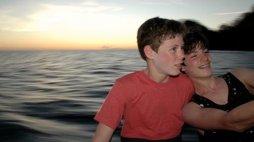 Portrait of friends on sea against sky during sunset