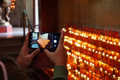 Close-up of human hands photographing illuminated candles with mobile phone