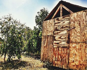 Old wooden structure amidst trees and plants in field against sky