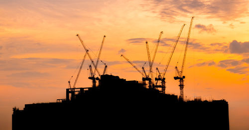 Low angle view of silhouette cranes against buildings during sunset