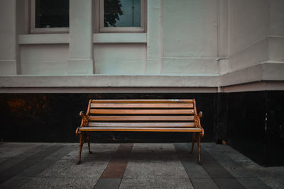 Empty bench by footpath against building