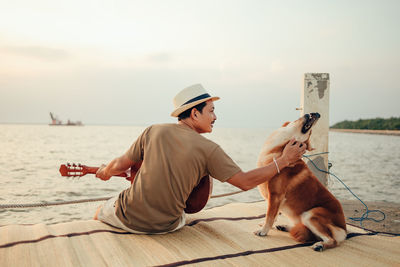 Rear view of man sitting with dog on pier against sea