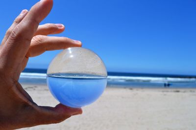 Cropped hand of person holding crystal ball at beach