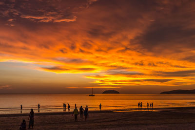 Silhouette people on beach against sky during sunset