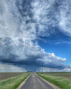 Country road amidst field against sky