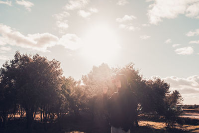 Rear view of woman standing by trees against sky