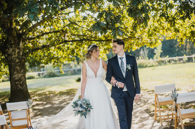 Bride holding bouquet while walking with groom in park