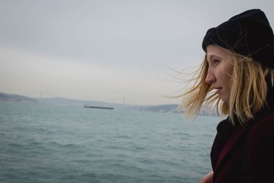 Side view of young woman by sea against sky