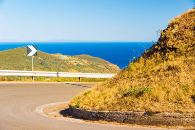 Road by sea against clear blue sky