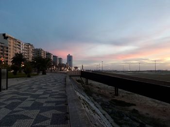 Road amidst buildings against sky during sunset