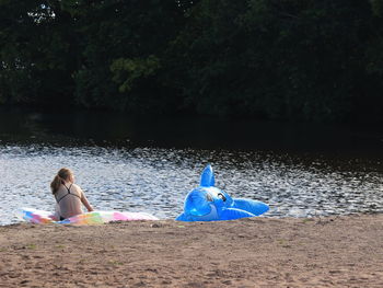 Rear view of women sitting on land by lake