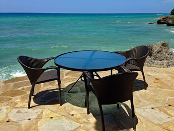 Empty chairs on table by sea against sky