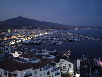 High angle view of illuminated city by sea against sky