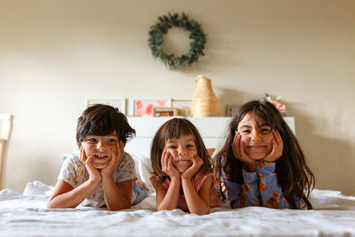 Group of smiling children laying in parent's bed holding face in hands