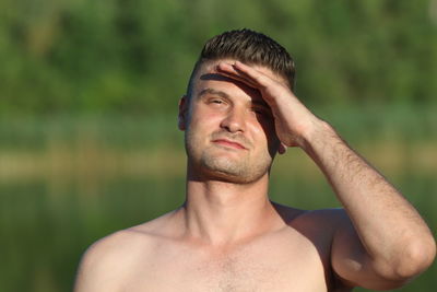 Close-up portrait of shirtless man shielding eyes in forest