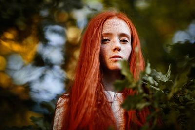 Low angle portrait of serious young woman standing by plant