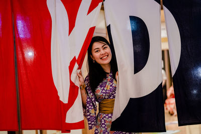 Portrait of smiling young woman standing against red wall