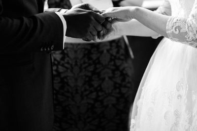 Midsection of bridegroom wearing wedding ring to bride in ceremony