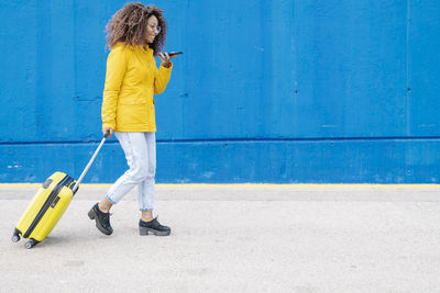 Full length of woman with umbrella standing against blue background