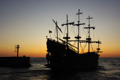 Silhouette ship moored at harbor against clear sky