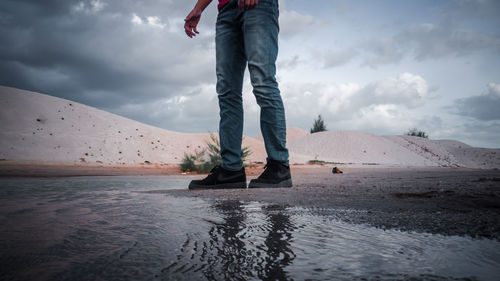 Low section of man standing at sea shore against sky