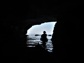 Silhouette man on rock in sea against sky