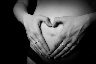 Close-up of woman with hands in heart shape on pregnant belly