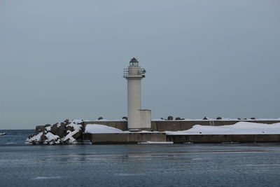 Lighthouse by sea against clear sky