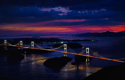 Illuminated bridge over river against sky at sunset