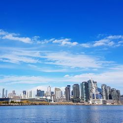 Sea by cityscape against blue sky