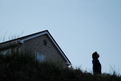 Surface level of woman standing by house against clear sky during sunset