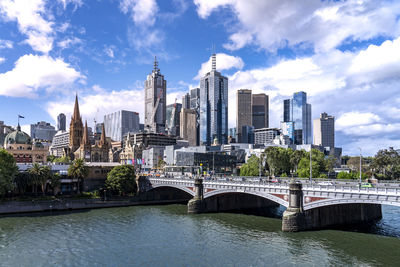 Bridge over river by buildings against sky in city