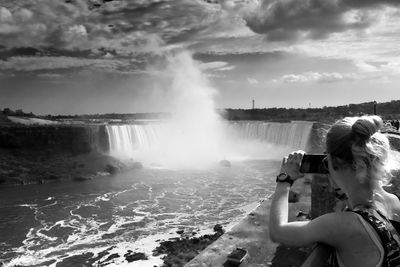 Rear view of woman photographing niagara falls against sky