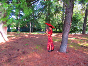 Full length of woman standing by tree trunk in forest