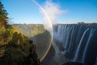 Scenic view of waterfall against rainbow in sky