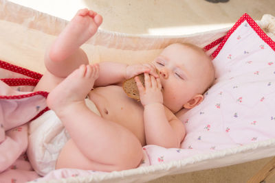 High angle view of cute baby girl with bread lying on bed