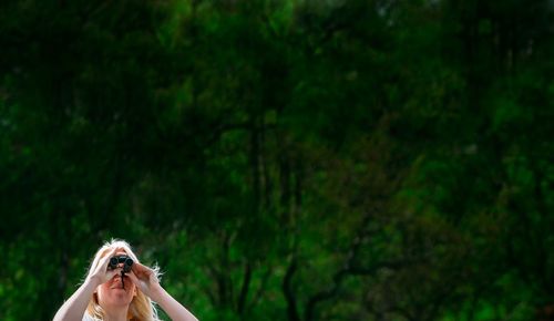Woman looking through binoculars against trees