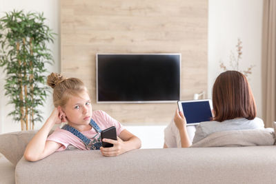 Woman using digital tablet while sitting by daughter on sofa at home