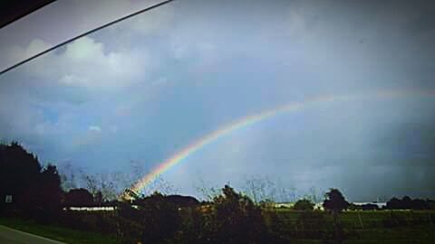 Rainbow over landscape against cloudy sky