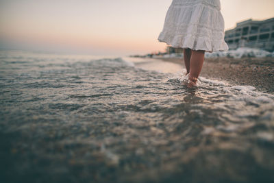 Close-up of barefoot child walking in shallow waves at sunset