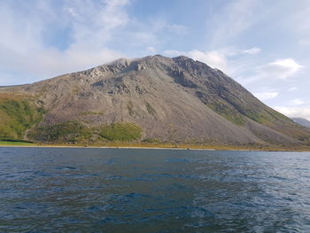 Scenic view of sea by mountain against sky