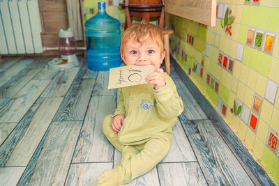 Funny baby in green clothes holds a sign of 10 months old milestone card in his mouth 10